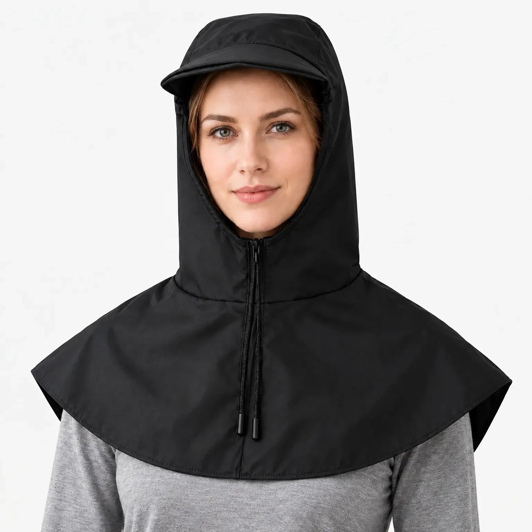 Front view of a black hooded cape with zip, drawstring cords and short brim, worn over a grey top against white. 7