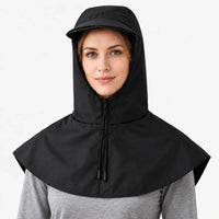 Front view of a black hooded cape with zip, drawstring cords and short brim, worn over a grey top against white. 7