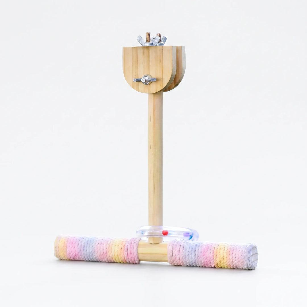 Wooden T-shaped perch with pastel rope-wrapped crossbar, a clear ring with coloured beads and wing-nut clamp at the top, on white. 1