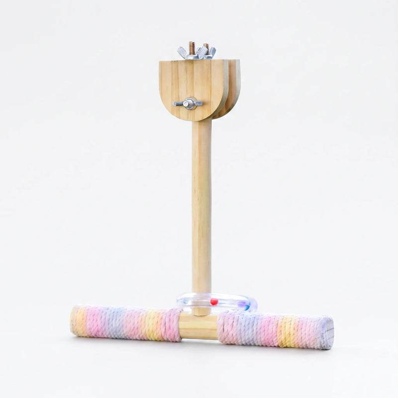 Wooden T-shaped perch with pastel rope-wrapped crossbar, a clear ring with coloured beads and wing-nut clamp at the top, on white. 1