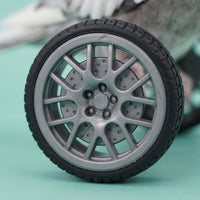 Close-up of one wheel showing its grey multi-spoke rim and black treaded tyre, with the bird blurred behind. 3