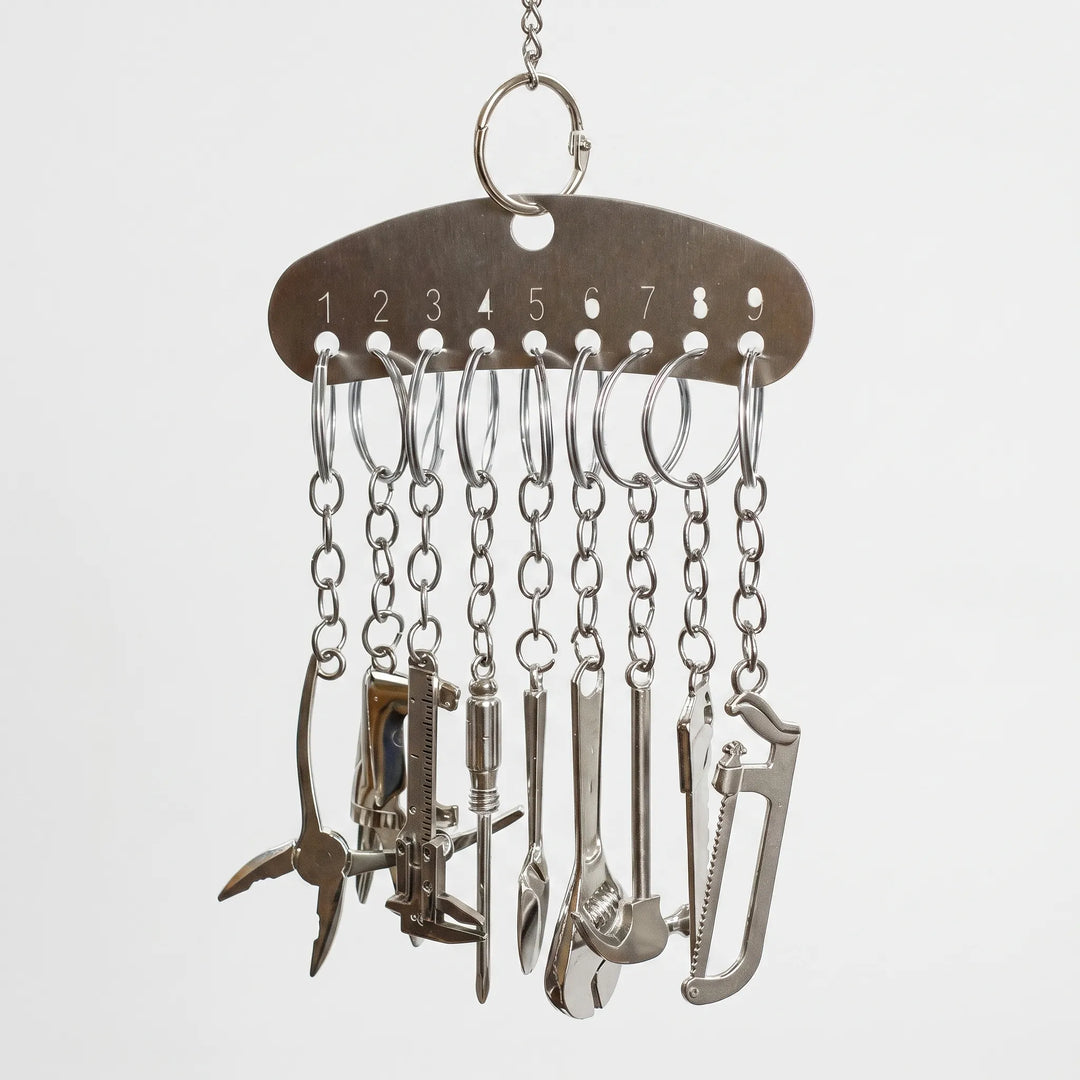 Metal bar hanging from a chain, with nine split rings and chains holding miniature metal tools such as pliers, a saw and a spanner. 1