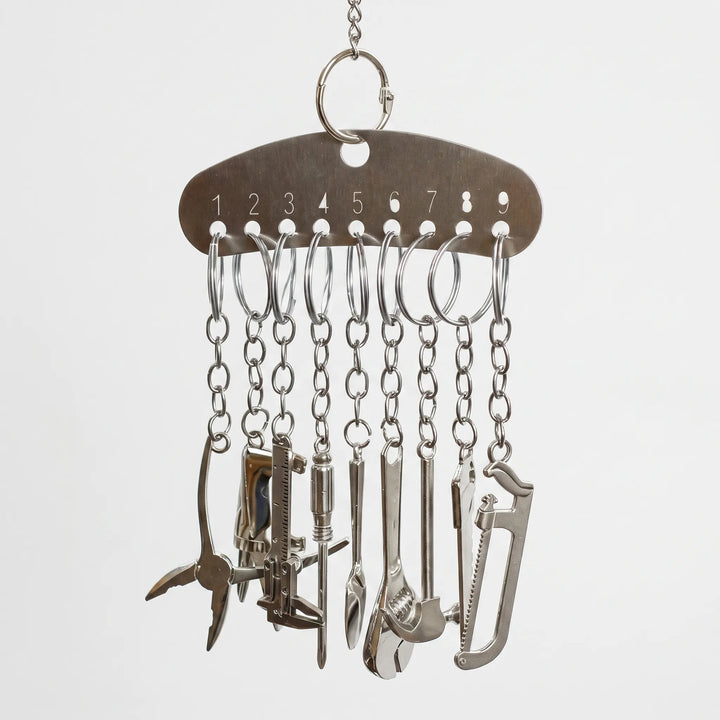Metal bar hanging from a chain, with nine split rings and chains holding miniature metal tools such as pliers, a saw and a spanner. 1