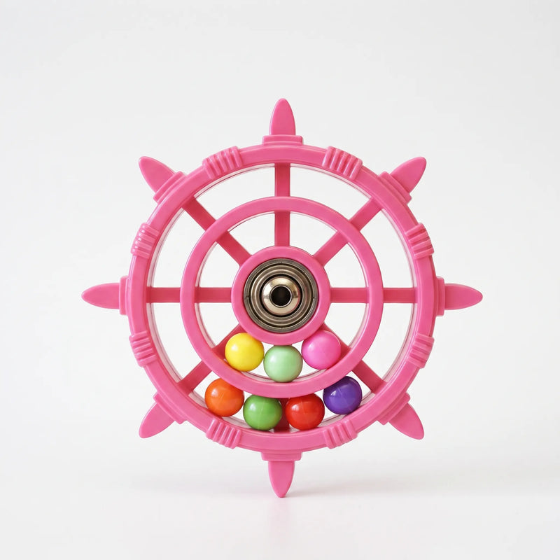 Pink ship's-wheel bird toy with a metal bearing hub and seven coloured balls, shown on a plain white background. 1
