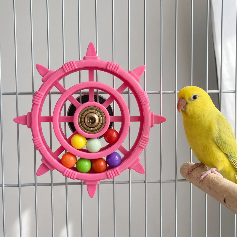 Pink wheel toy fixed to the bars of a cage, with a yellow parakeet perched on a wooden branch beside it. 2