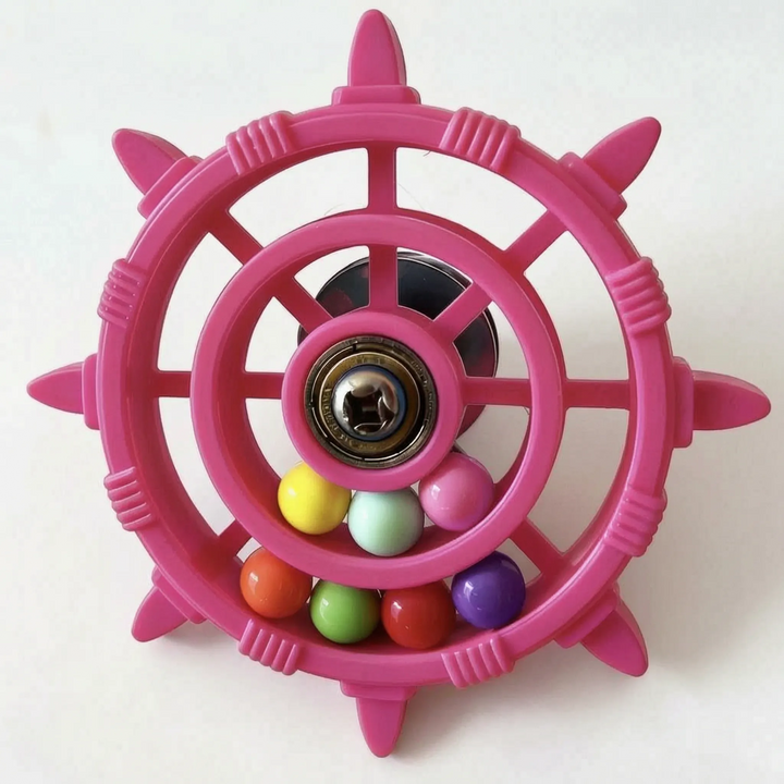 Pink wheel toy seen slightly from above, showing the dark suction cup behind the central bearing and the coloured balls. 4