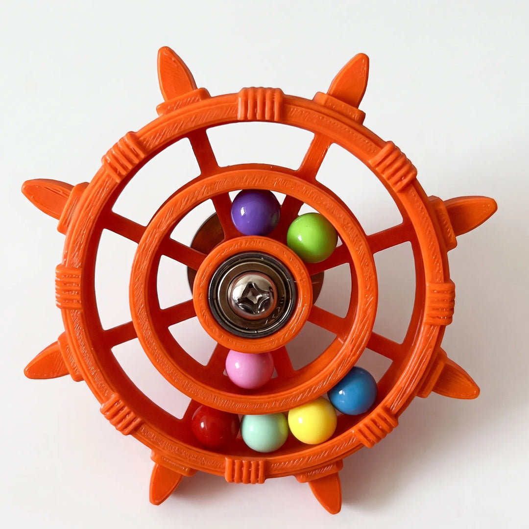 Orange version of the wheel toy with a visibly ridged plastic finish, a steel screw at the hub and seven coloured balls. 5