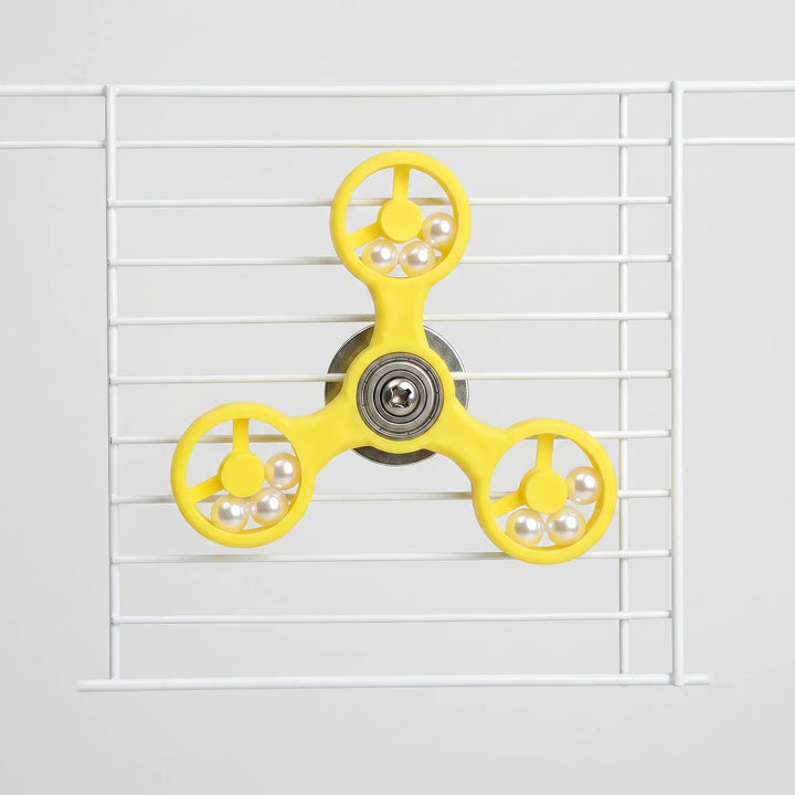 Front view of the yellow three-armed spinner toy fixed to white cage bars, with pearl beads in each ring. 1