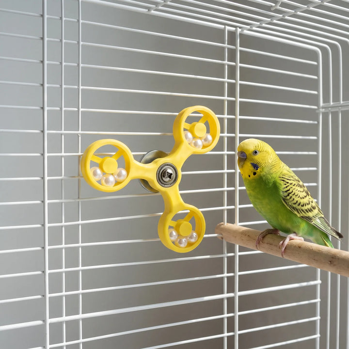Yellow spinner toy attached to a white cage, with a green budgerigar perched on a wooden perch next to it. 3