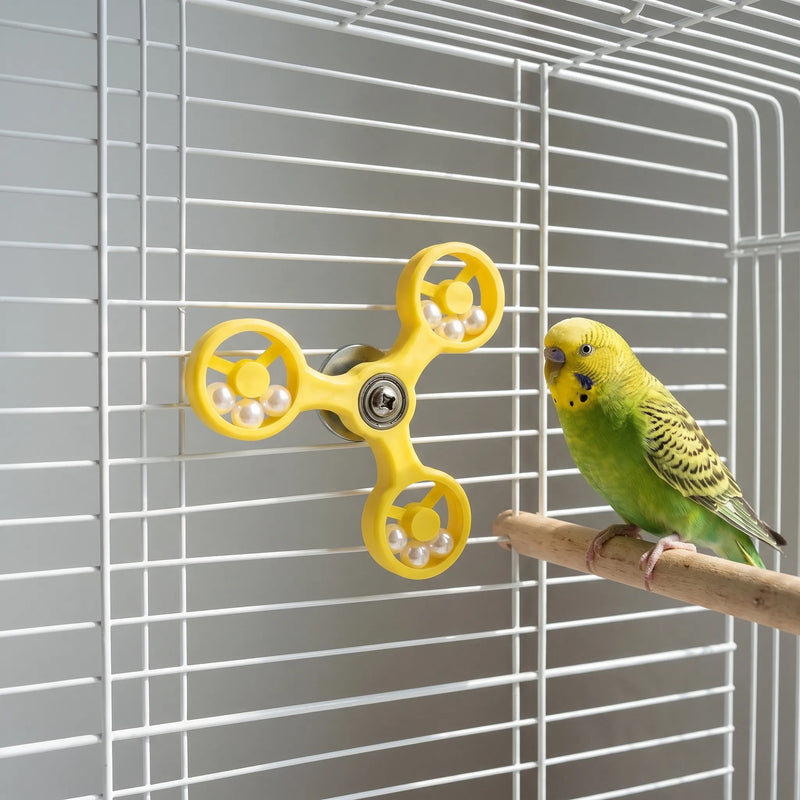 Yellow spinner toy attached to a white cage, with a green budgerigar perched on a wooden perch next to it. 3