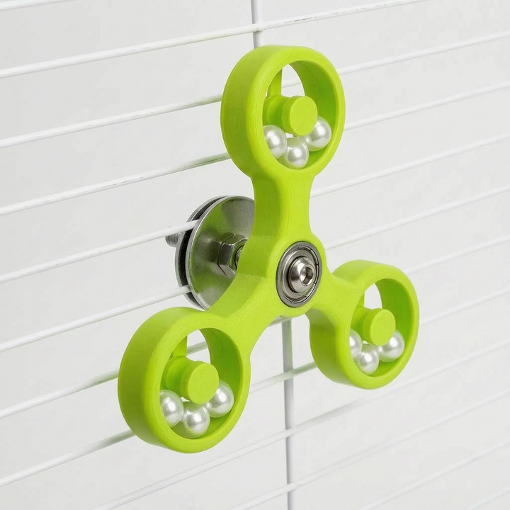 Lime green version of the spinner toy mounted on white cage bars, showing its metal fixing hardware at the back. 6