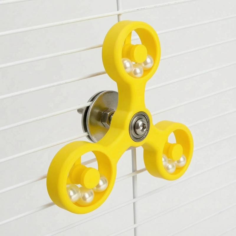 Yellow spinner toy seen at an angle on white cage bars, showing the washer and bolt fixing behind the arms. 7