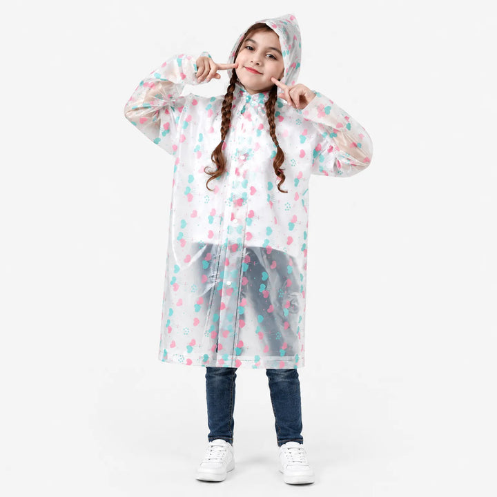 Smiling girl with braids poses in a clear raincoat printed with pink and teal heart balloons, hood up, on a plain background. 2