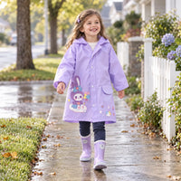 Girl in a lilac raincoat with a bunny-on-cloud print and lilac rain boots, walking happily along a wet sidewalk. 3