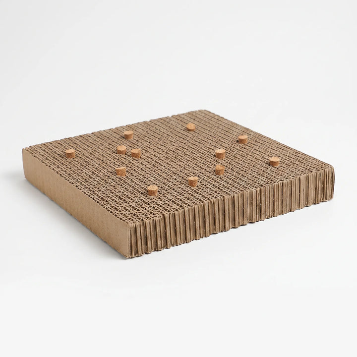 Corrugated cardboard platform with small cork stoppers pushed into its top, shown at an angle on a plain white background. 1