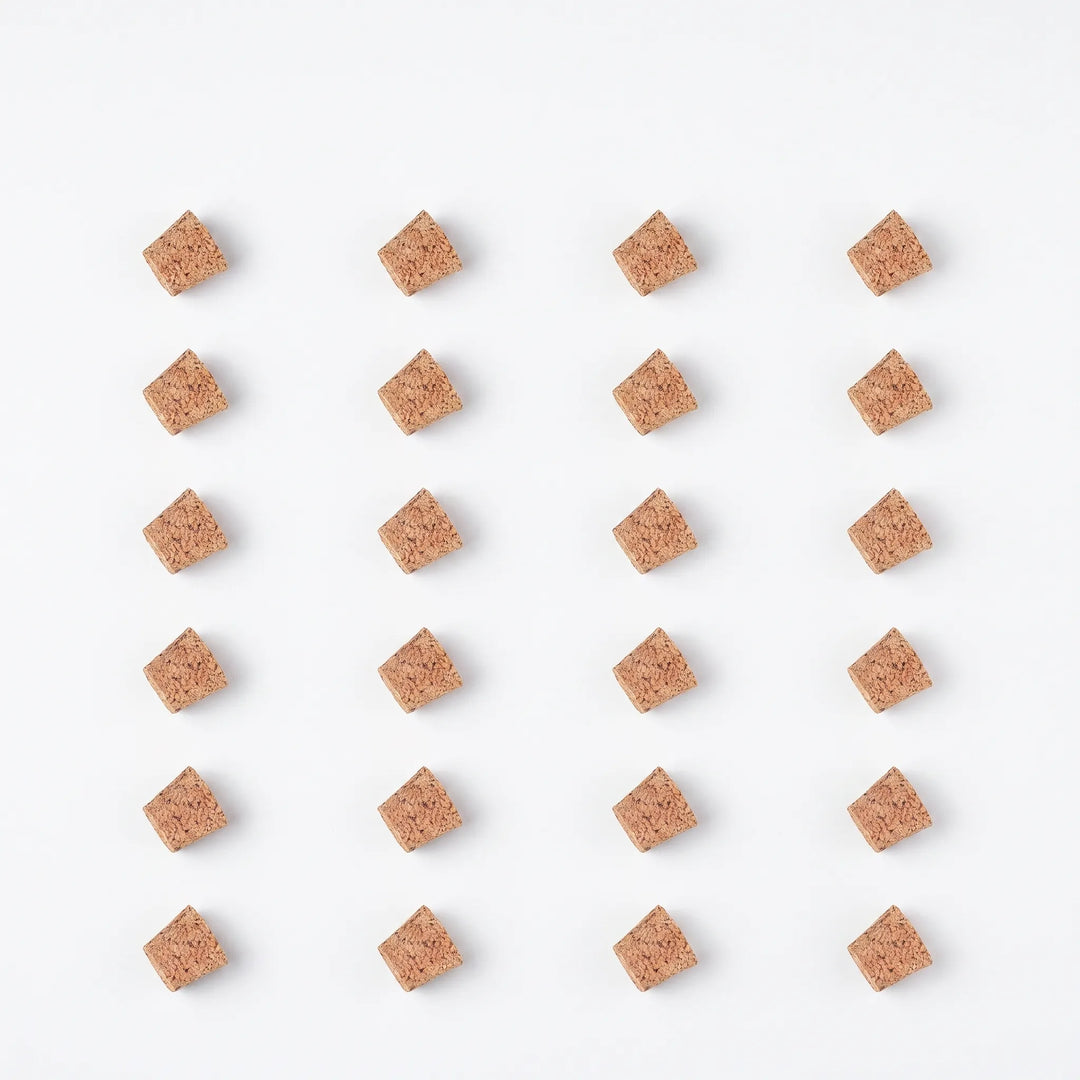 Flat lay of twenty-four spare cork stoppers arranged in a neat grid of rows on a white background. 9