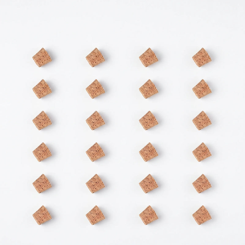 Flat lay of twenty-four spare cork stoppers arranged in a neat grid of rows on a white background. 9