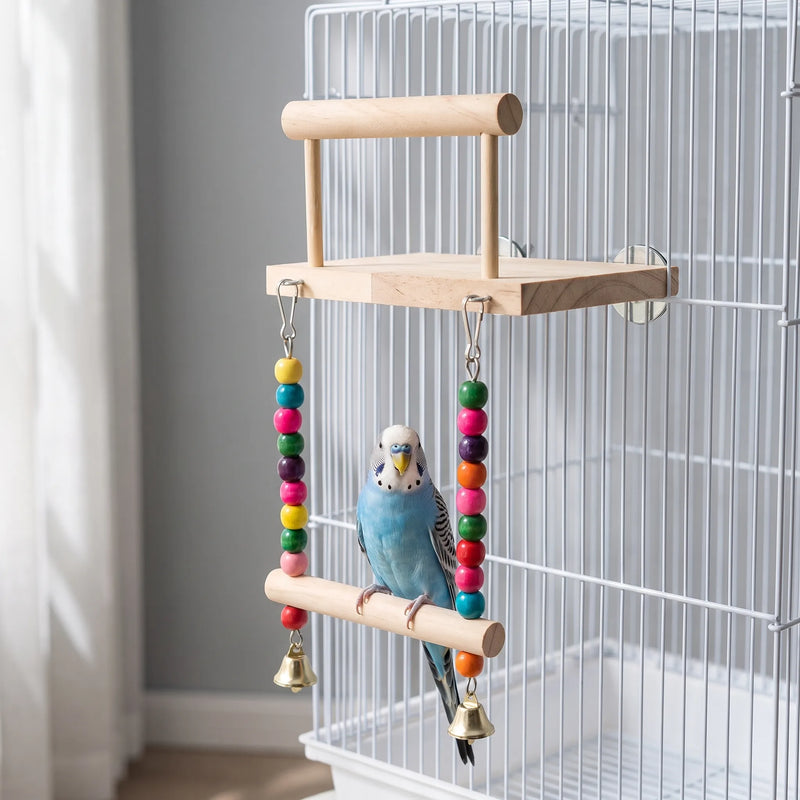 Blue and white budgie perched on the swing beneath the wooden platform, hung inside a white cage with colourful beads and bells. 2