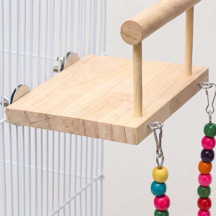 Close-up of the pale wooden platform, its metal discs and screws clamped to the cage bars, with hooks and coloured beads hanging. 3