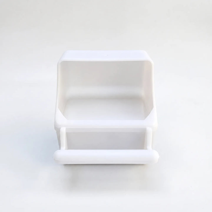 White plastic seed feeder seen from the front on a plain background, showing the open hood and the rounded perch bar. 1