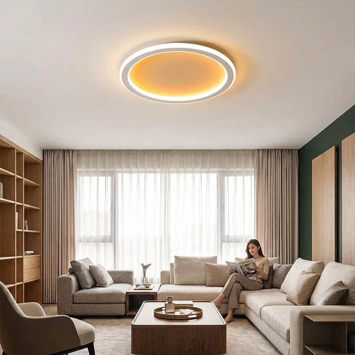 Round white ceiling light glowing warmly above a living room where a woman reads on a sofa 1
