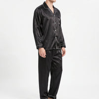 Three-quarter side view of a model in the black satin pyjama shirt and trousers, showing the button front and piping. 4