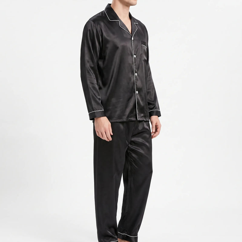 Three-quarter side view of a model in the black satin pyjama shirt and trousers, showing the button front and piping. 4
