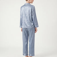 Back view of the blue satin pyjama set on a model, showing the all-over heart pattern on top and trousers. 3
