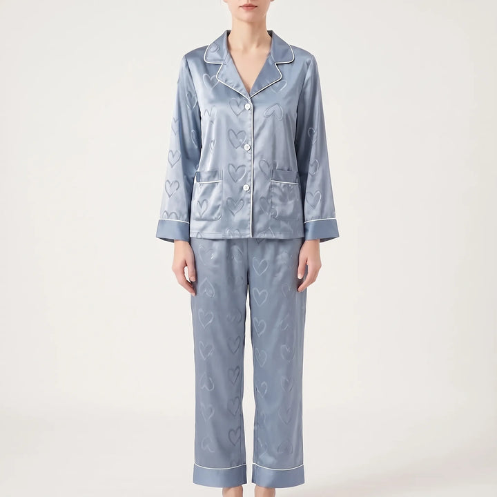 Front view of the blue satin pyjama set on a model with straight trousers, piped cuffs and heart jacquard pattern. 7