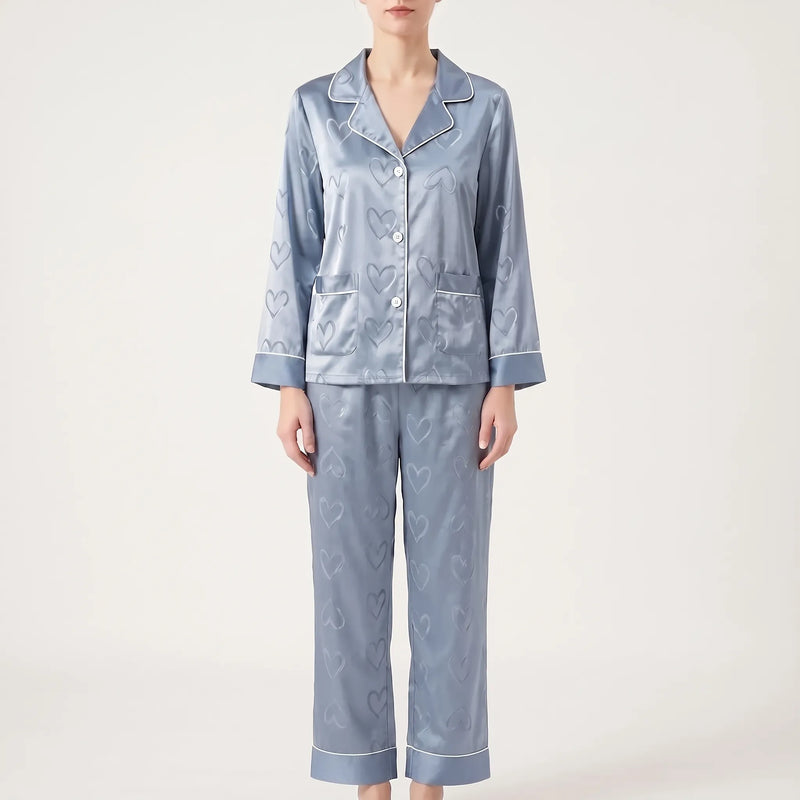 Front view of the blue satin pyjama set on a model with straight trousers, piped cuffs and heart jacquard pattern. 7