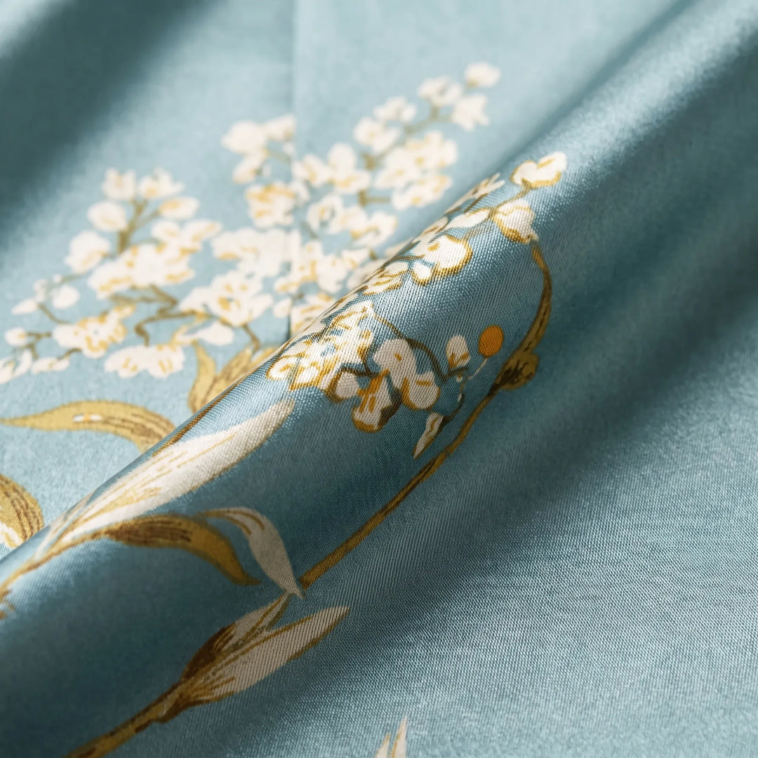 Close-up detail of the teal satin fabric with a draped fold, showing white and golden blossom print and subtle sheen. 4