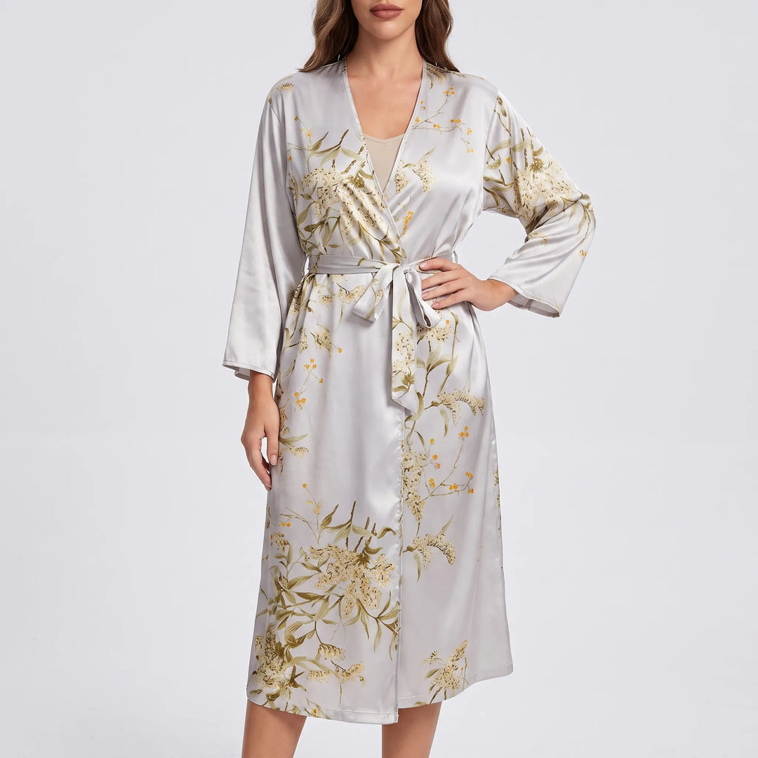 Model wearing the robe in a light silver-grey satin with golden floral print, belted at the waist, one hand on hip. 5