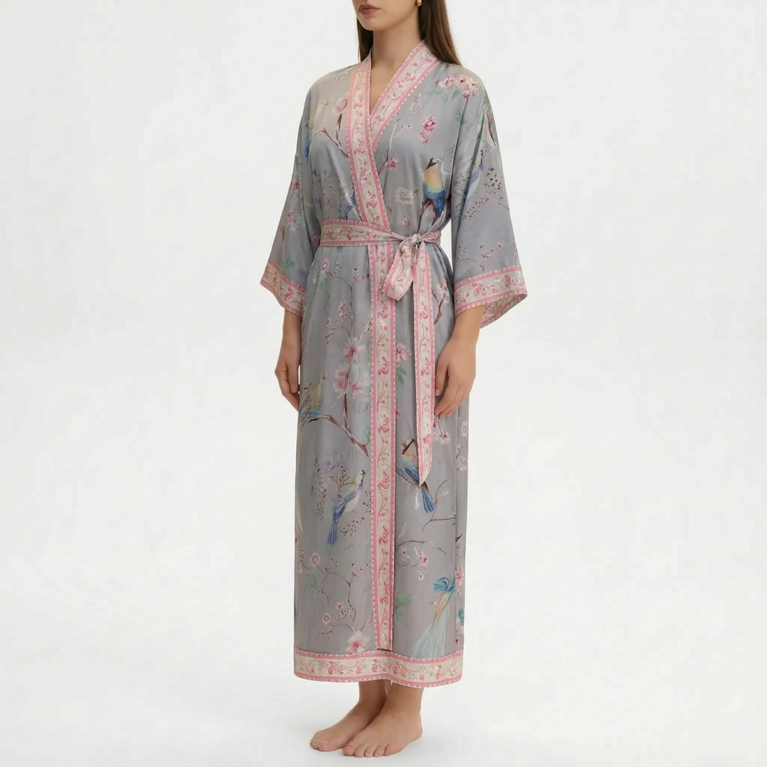Model wearing the long wrap robe in grey with birds and blossoming branches print and a pink floral border. 14