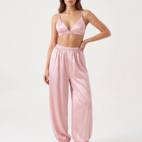 Model with one hand on her hip in the pink satin bralette and gathered-waist jogger-style pants, studio front view. 2