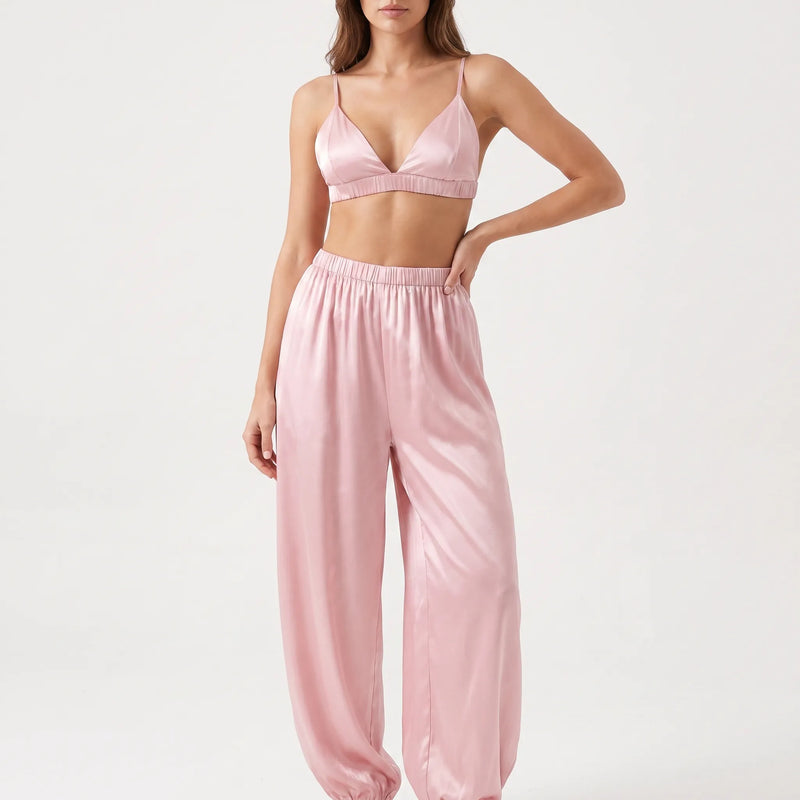 Model with one hand on her hip in the pink satin bralette and gathered-waist jogger-style pants, studio front view. 2