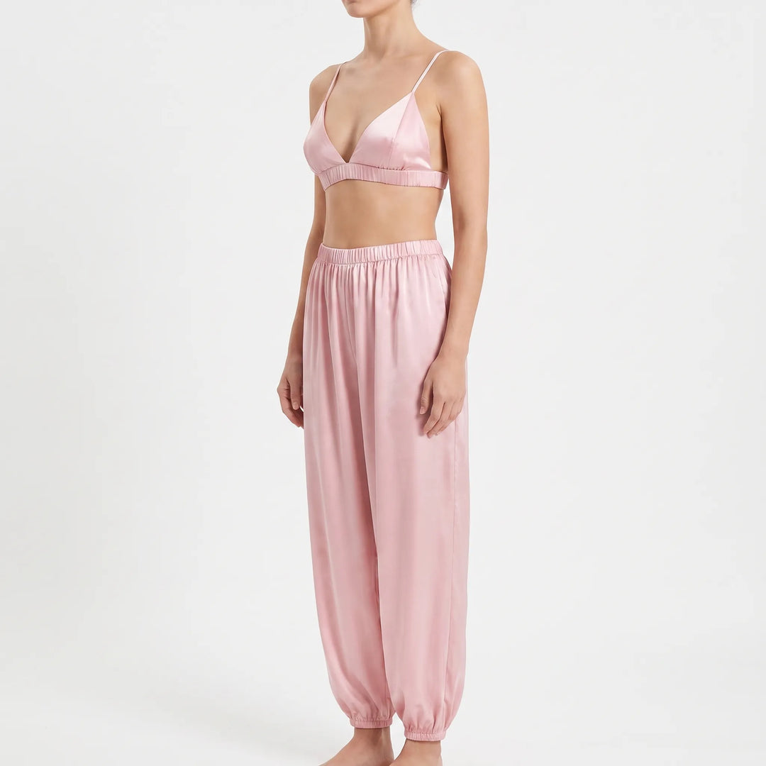 Three-quarter side view of the pink satin bralette and relaxed trousers with elasticated waist and ankle cuffs, worn by a model. 4
