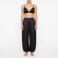 Model in the black satin version of the triangle bralette and wide balloon-leg trousers with elastic waist, front view. 6
