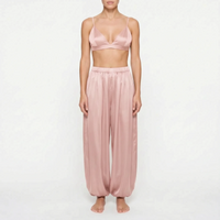 Model wearing the dusty rose satin version of the bralette and wide, gathered trousers, front view on a plain background. 7