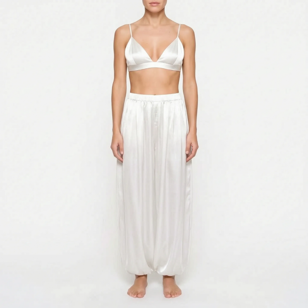 Model wearing the white satin version of the triangle bralette and full gathered trousers, front view on a plain background. 8