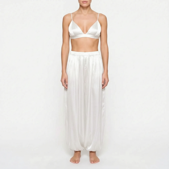 Model wearing the white satin version of the triangle bralette and full gathered trousers, front view on a plain background. 8