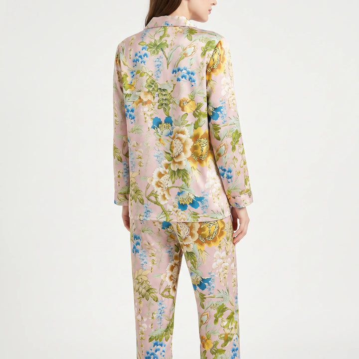 Back view of a model wearing the floral pyjama set, showing the large yellow, blue and white botanical print across the shirt and trousers. 2