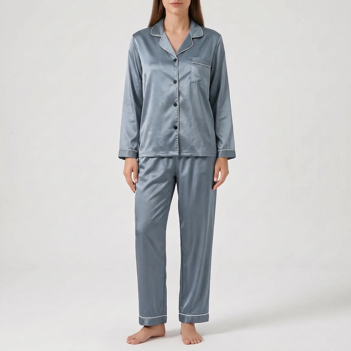 Model wearing the satin pyjama set in slate blue-grey with white piping and dark buttons, front view. 9