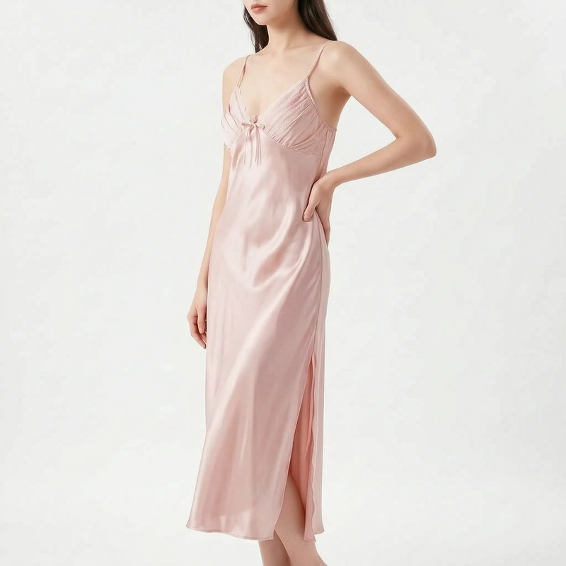 Model with hand on hip wearing the nightdress in soft blush pink satin, with pleated bodice, bow and side slit. 7