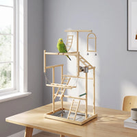 Wooden bird playground standing on a table in a bright room, with a green budgie perched on a middle bar. 2