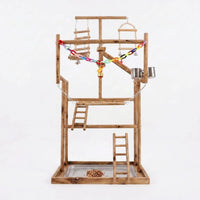 Multi-level wooden bird playground on a plain white background, with ladders, swings, a colourful chain, bells, steel cups and a seed tray. 1