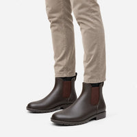 Brown Chelsea rain boots with brown elastic panels worn with beige trousers, seen from a slightly raised angle on white. 5