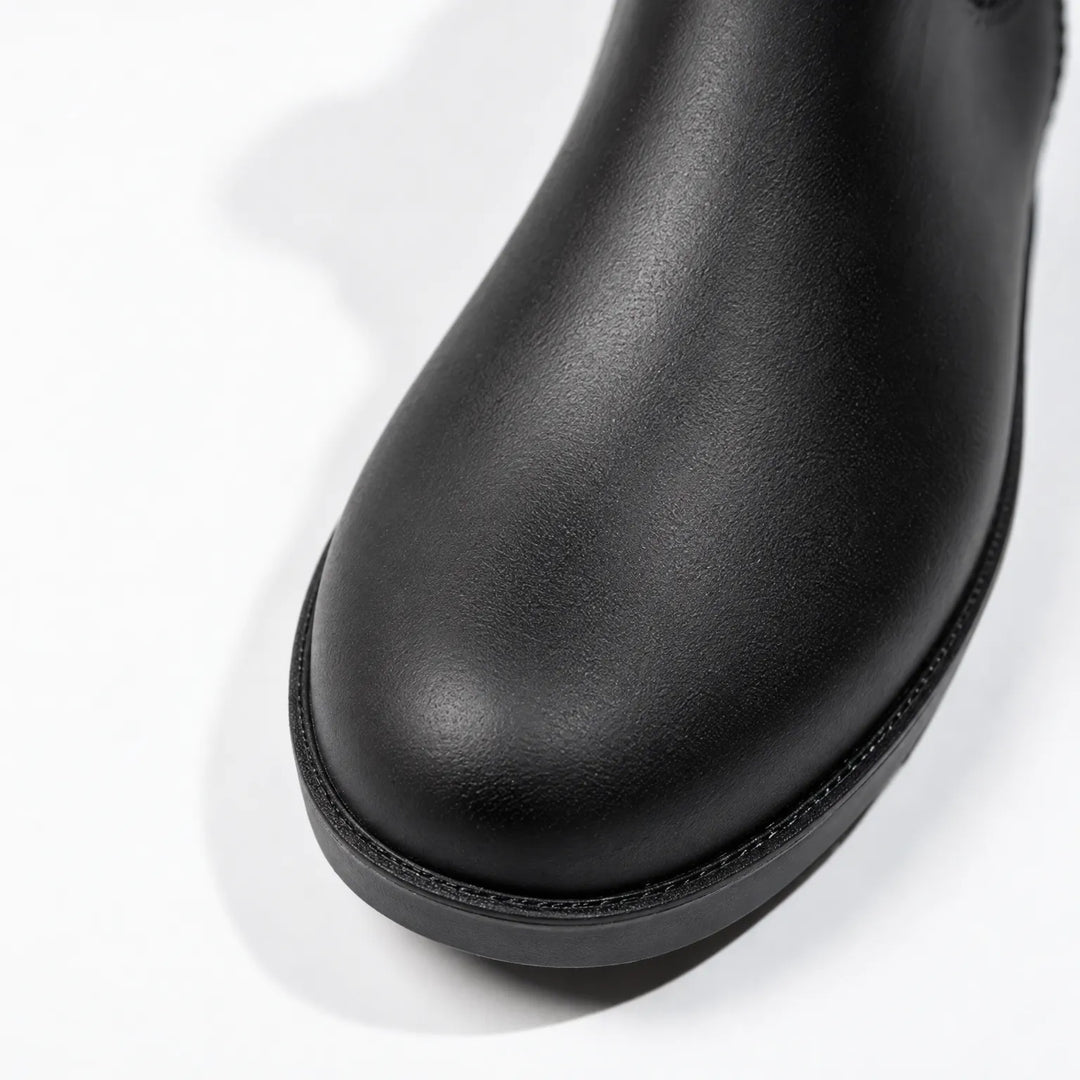 Close-up of the rounded toe of a black rain boot, showing its textured matte surface and stitched edge above the sole. 6