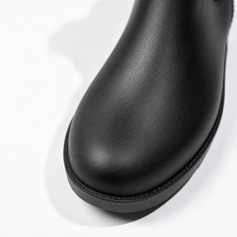 Close-up of the rounded toe of a black rain boot, showing its textured matte surface and stitched edge above the sole. 6