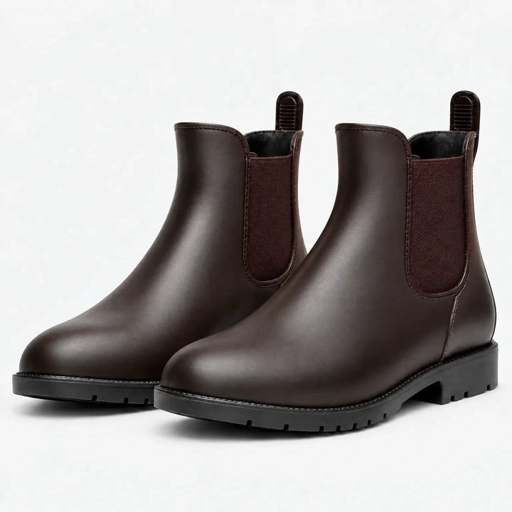 Pair of brown Chelsea rain boots with brown elastic panels, pull tabs and black treaded soles, shown at an angle on white. 7