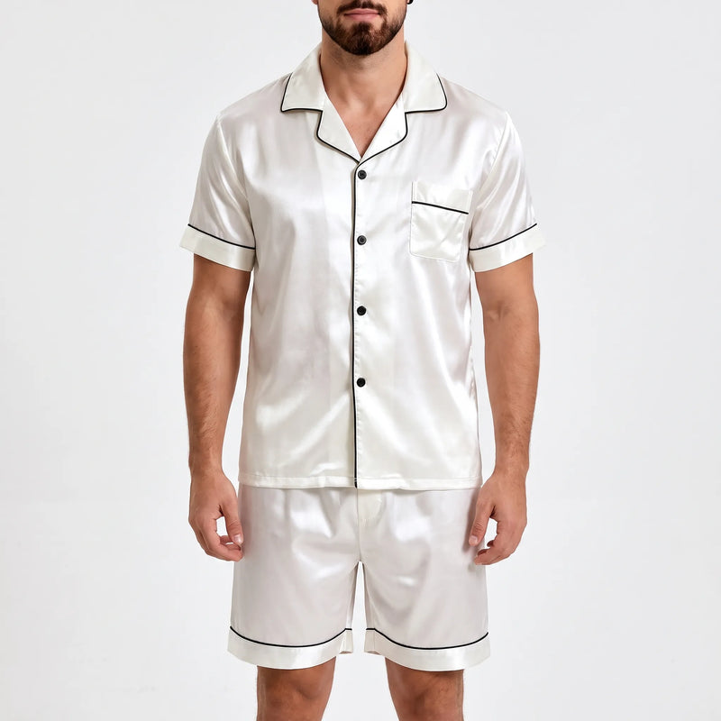 Front view of white satin pyjama shirt and shorts with black piping, worn by a bearded model against a plain light background. 2